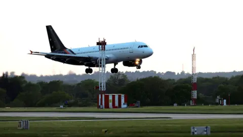 EPA A plane with a white body and blue tail with white stars is seen landing from the side on a runway against a bright sky.