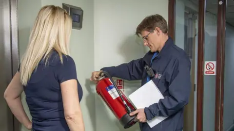 A man looking at a fire extinguisher whilst a woman looks on