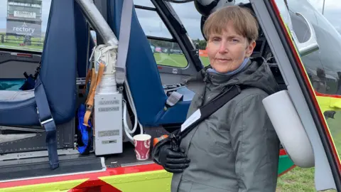 Helen Hide-Wright Helen Hide-Wright with her arm in a sling stood by an air ambulance. 