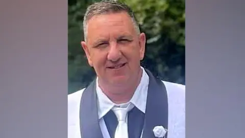 Man in a grey suit and white shirt posing for a picture. He is clean shaven, with short receding grey hair.