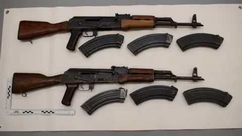 Greater Manchester Police Two rifles surrounded magazines on a white background
