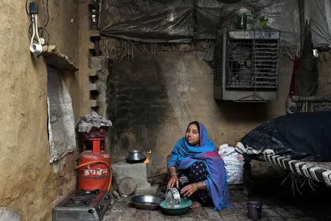 Bloomberg via Getty Images A woman prepares food to be cooked on a liquefied petroleum gas (LPG) connected stove at her home in a village near Modinagar, Uttar Pradesh, India, 