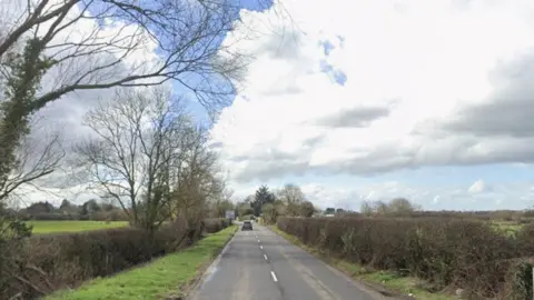 A screenshot taken from Google Maps showing Old Gloucester Road in Staverton. Image shows a country road with grass and hedges on either side.