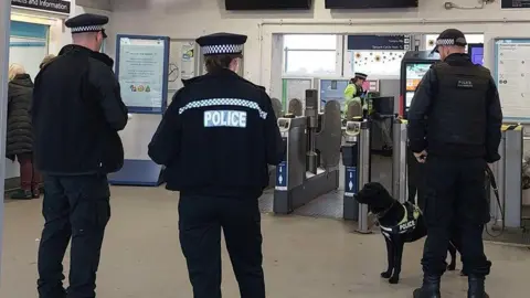 Three Kent Police officers in all black at a train station entrance