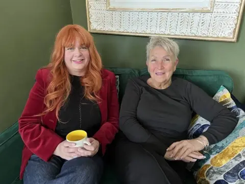 Co-directors Glinda Bishop and Jackie Cousins sit on a green sofa at Mrs. Slocombe's Cat Cafe in Chatham