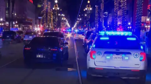 Police cars with blue lights line the scene of the incident in New Orleans' French Quarter during night time hours 