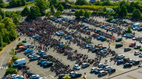 Ross Bisley An aerial image showing hundreds of people gathered in a car park. There are lots of motorbikes parked in spaces.