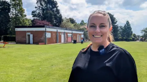 Josh Gorroño Chapman/BBC Woman looking down lens in front of flat-roofed brick building in sunny park