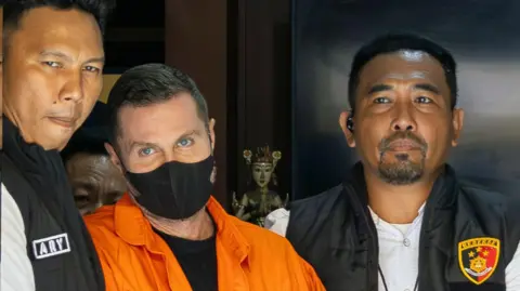 EPA Lyons flanked by police officers as he was led from a Bali police station before being deported in March