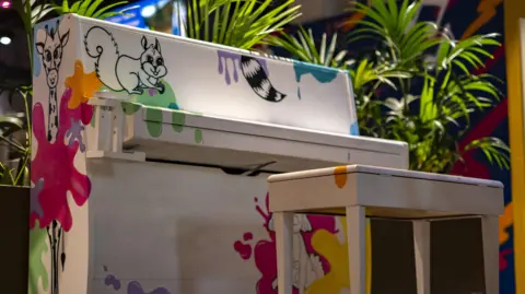 Bradford Council A multi-coloured upright piano with a white base coat and animal line drawings