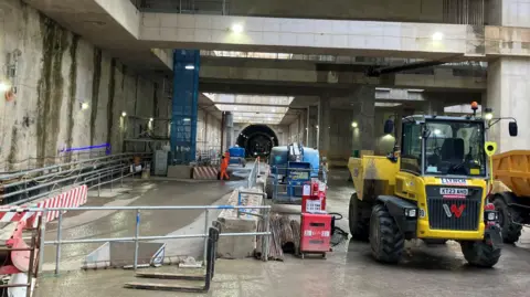 A construction site with a dump truck. In the distance there is a large black hole where the boring machines will eventually go to Euston.