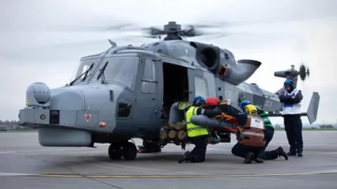 A Wildcat Helicopter being attended to by crew on a runway with its propellers spinning