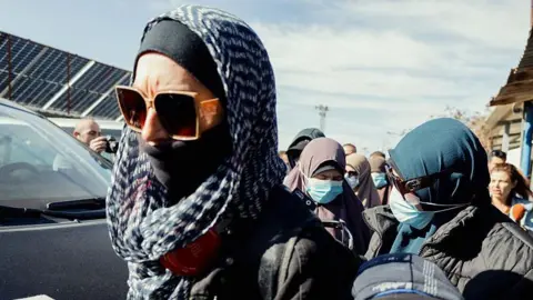 Getty A woman in a headscarf and dark glasses with other women in headscarves and faces masks behind her.