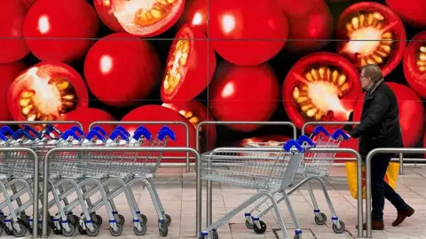 A man pushes a supermarket shopping trolley next to a wall decorated with a large picture of sliced in half cherry tomatoes