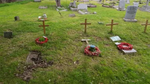 Neil Stanlake The current graves of the firefighters who died. There are four wooden crosses, three of which have poppy wreaths laid below them.