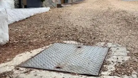 A general view of a cesspit on a stone driveway.