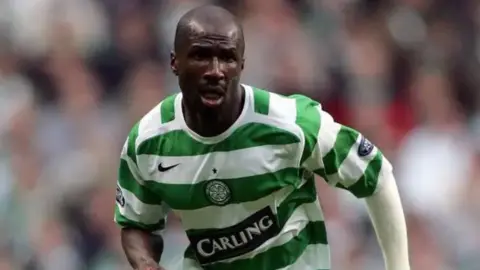 AFP via Getty Images Mr Camara is pictured in a Celtic top in a match running on the pitch. He has what looks like a white bandage on his left arm.