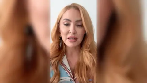 Natasha Hamilton has long red hair and is wearing a blue and white top.