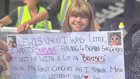 Amy Evie-Mae holding a sign which says: "Lewis, when I was little I had to 'Survive' having four brain surgeries. It left me with 'Bruises'. You're my first concert as I think music is 'Pointless' without you so 'Before You Go' please have a photo with me as I'm not ready for you to 'Forget Me' and 'I Wish You the Best'. 