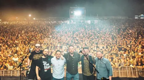 Oscar Bradley The band standing next to each other on stage with the crowd behind him.
