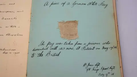 Hansons Auctioneers Page of the album showing a small piece of rough white material sewn to the page, with handwriting around it describing what it is and where it was gathered.