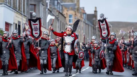 Reuters Lynden Nicolson the Guizer Jarl, and his squad, including children, march in Viking costumes during daylight