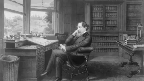 Getty Images A contemporary black and white portrait of Charles Dickens, an old man with a beard, sitting at a desk in a room full of books in a country house. He is sitting with one hand resting on the arm of his chair and his head propped on his other hand.
