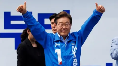 Lee Jae-myung raises two thumbs up while wearing a blue jacket printed with the number one - the number representing his candidacy.