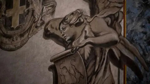 Getty Images A close-up shot of a painted grey angel. Its face resembles that of Italian Prime Minister Giorgia Meloni. She has wings and holds a scroll on which the shape of Italy is drawn.