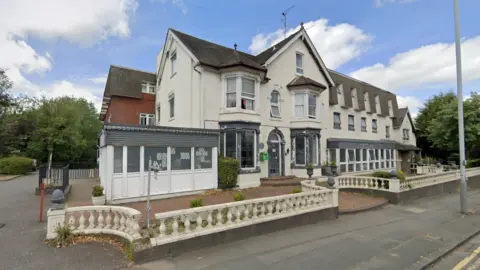 The former Goldthorn Hotel in Penn Road, Wolverhampton is mainly white with a low concrete railing around the front of it and some greenery on show. It is next to a road and a property can be seen behind it.
