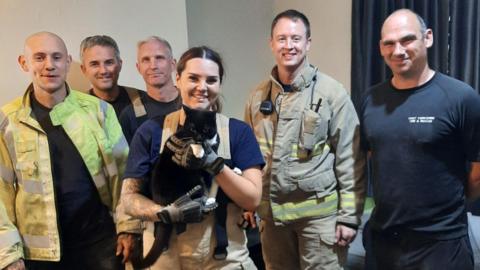 A fire crew pictured with one firefighter holding a black and white cat