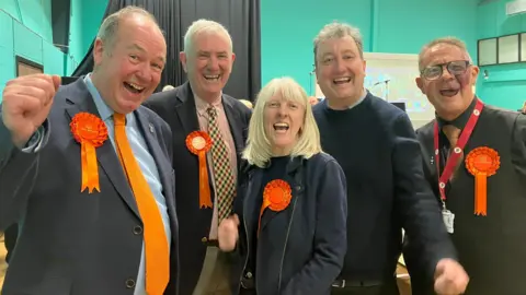 Orange rosette-wearing councillors celebrate their success in the West Lancashire Council election