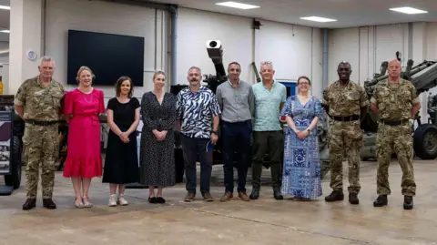 Swindon Borough Council Several members of the military next to some councillors. All are standing in a line, and there is an artillery gun behind them
