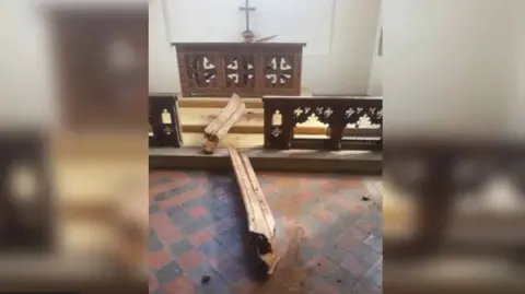 James Woodhouse A wooden beam broken in two, on top of floor tiles on an aisle.  