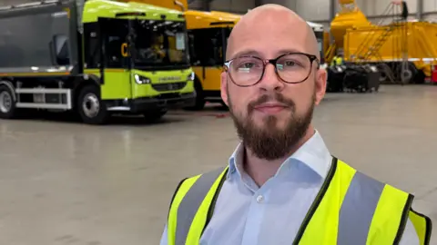 A bald man with black glasses. He is wearing a white shirt and a yellow hi-vis jacket