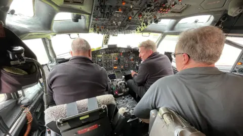 Inside a Boeing 727 plane's cockpit with three men.