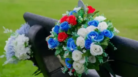 White and blue memorial flowers tied to a bench