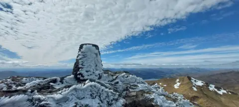 Arunava Ghosh-Ray The snow covered summit of a mountain with a blue cloudy sky