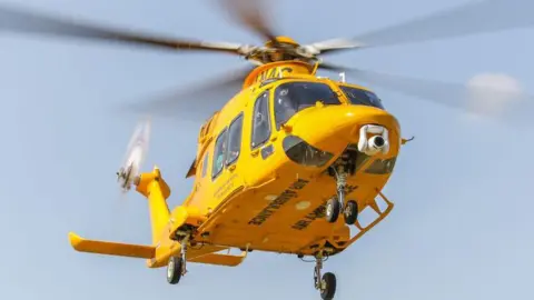 A yellow air ambulance helicopter in flight