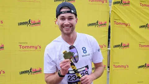 Getty Images AJ Pritchard smiles while holding up his finisher's medal in front of a yellow London Landmarks Half Marathon backdrop