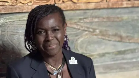 A woman wearing a black blazer with a badge on the lapel, reading "Surrey Day".