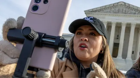 A woman holding a phone on live stream in front of the Supreme Court 