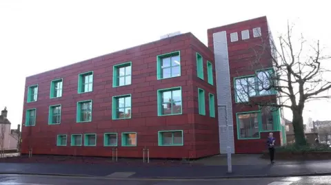 Voreda House office block in Penrith. The three-storey red building has green windows and is made up of a main block, with a tower next to it, in the same style and colours.