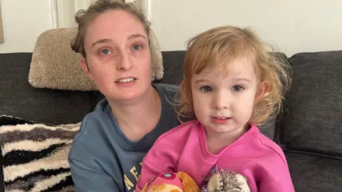 A picture of Emily and her daughter. She is wearing a grey jumper and her daughter has a pink jumper.