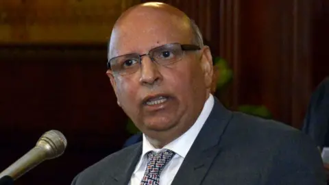 Getty Images Mohammad Sarwar, who is bald with glasses, speaks into a microphone. He is wearing a dark suit, white shirt and patterned tie. 