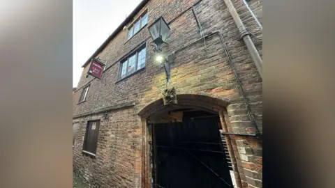 Apple FM An old gatehouse in a town centre, a three-storey brick building with a large arch. 