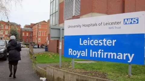 PA Media A sign outside the Leicester Royal infirmary with a person walking by in the background