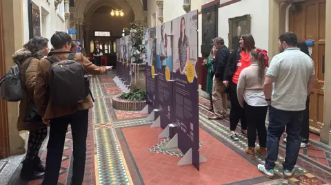 Jessica Bayley/BBC People looking at photos and information displayed as part of the exhibition.