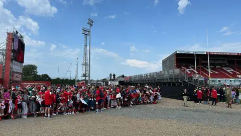 Matt Dean/BBC Fans in red and white stand behind barriers as players sign autographs outside the ground
