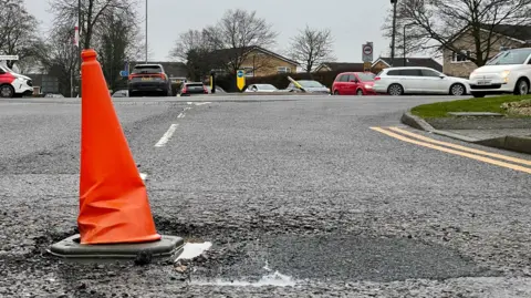 An orange traffic cone in a pothole to warn motorists